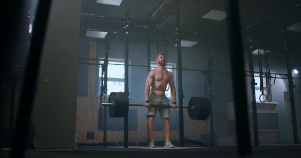 Jongeman doet de clean en jerk gewichtheffen oefening in de sportschool. Een man die nachtelijke oefeningen doet in de sportschool. Jonge atleet tilt lange halter op zijn borst. Mannelijke gewichtheffer tilt een lange halter op een wedstrijd — Stockvideo