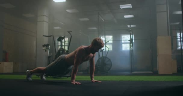 Sterke en fitte atletische man in Sport Top en Shorts doet push-up oefeningen in een Loft Style Industriële Gym met motiverende posters. Het maakt deel uit van haar Cross Fitness Training Workout. — Stockvideo