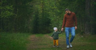Baba ve oğul el ele tutuşarak parkta yürüyorlar. Mutlu baba, sevgili oğluyla parkta yürüyor.