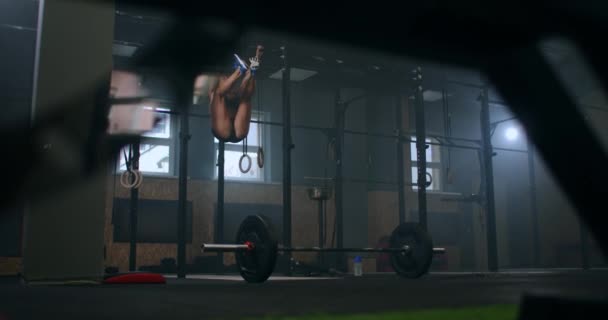 Movimiento lento: Levantar los pies hasta la barra en la barra de gimnasio, ejercicio atractivo mujer muscular y entrenar en el gimnasio. Mujer atleta de pie en una barra horizontal levanta las piernas para entrenar los músculos de los abdominales — Vídeos de Stock