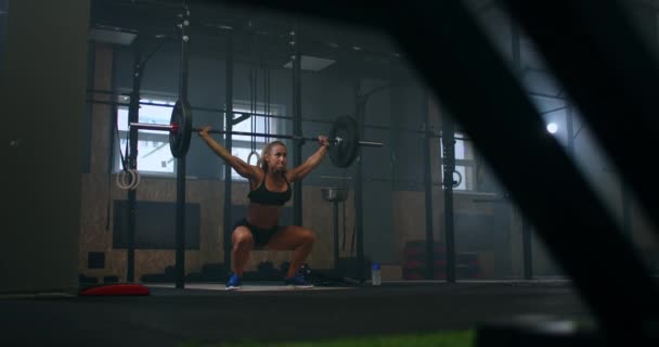 Langzame beweging: Training squats met halters over het hoofd. Gespierde vrouwelijke heffen lange halter over hoofd training schouders in de sportschool. Zelfverzekerde fitnessvrouw die krachttraining beoefent met zwaar materieel. — Stockvideo