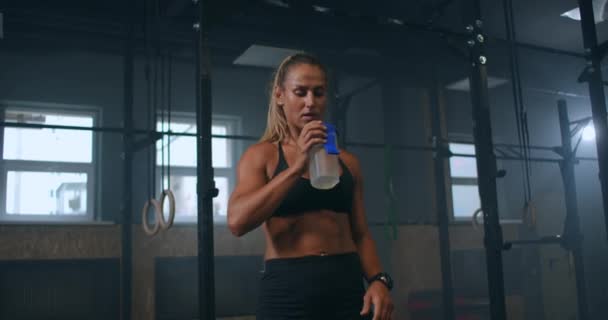 Sportliche Frau im Fitnessstudio, die nach dem Training eine Flasche Wasser trinkt und den Puls auf der Sportuhr kontrolliert. Herzfrequenzmessung — Stockvideo