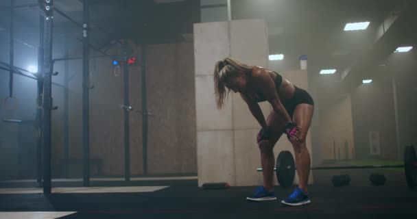 Mujer cansada y agotada después de un duro entrenamiento en el gimnasio está sentada en el suelo y respirando duro. Atleta profesional se está preparando para las competiciones. El trabajo duro y la superación de sí mismo, y el dolor . — Vídeo de stock