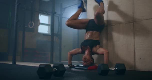 Silná žena provádí svertical kliky stojící na hlavě v tělocvičně. provádět push-UPS vzhůru nohama. push-UPS proti zdi vzhůru nohama — Stock video