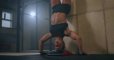 Güçlü bir kadın spor salonunda başının üstünde dikey şınav çeker. Baş aşağı şınav çek. Yukarı itişleri duvara ters çevirin.