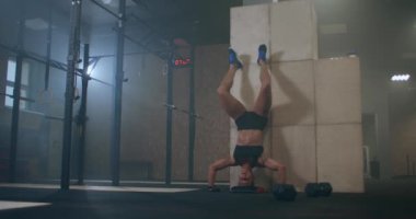 Güçlü bir kadın spor salonunda başının üstünde dikey şınav çeker. Baş aşağı şınav çek. Yukarı itişleri duvara ters çevirin.