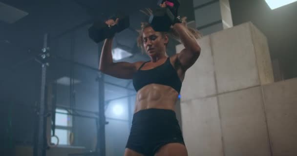 Жінка піднімає гантелі над головою під час тренування. Підняття ваги. Важка підготовка в спортзалі . — стокове відео