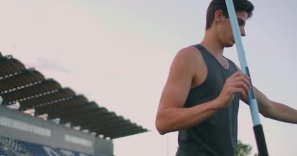 Cansado lanzador de jabalina un hombre en el estadio recoge lanzas. Preparándose para el todoterreno. Caminar por el estadio después de entrenar en el fondo de las gradas y llevar lanzas para lanzar. — Vídeos de Stock