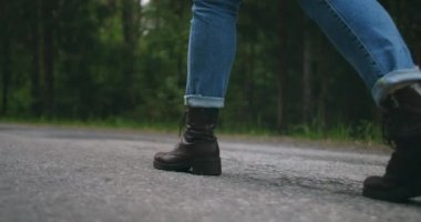 Yavaş çekimde yakın plan çekimde, siz gezgin ayakkabılar yolda kot pantolonla yürüyorsunuz. Ayakkabılar asfaltta bir orman yolunda gider.