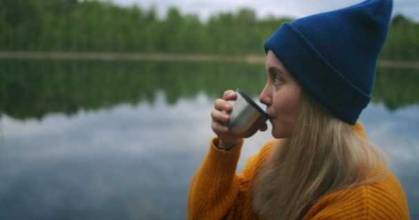 一位女旅行家背着背包喝茶，欣赏坐在木制码头上的山林湖水美景。一个孤独女人孤独旅行的慢动作概念。检疫和旅行 — 图库视频影像