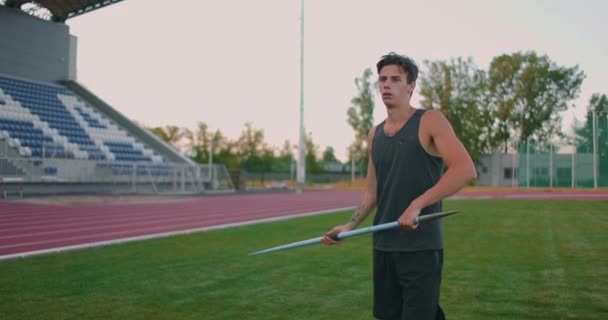 Cámara lenta: un atleta masculino en el estadio se concentra y se prepara para hacer un lanzamiento de jabalina. Actitud y expresión seria. Va por ahí recogiendo lanzas. Formación de un lanzador de jabalina — Vídeos de Stock