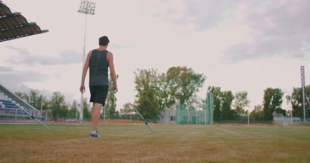 Ένα ακόντιο Ο Thrower περπατά γύρω από το γήπεδο με λόγχες και τις συλλέγει. Πηγαίνετε με ένα δόρυ στο χέρι στο παρασκήνιο του γηπέδου στέκεται. Η προπόνηση του Ολυμπιονίκη. — Αρχείο Βίντεο