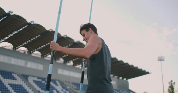 Fáradt gerelydobáló, egy férfi a stadionban lándzsákat gyűjt. Felkészülök a körökre. Séta a stadionban edzés után a háttérben a lelátók és a hordozó lándzsák dobás. — Stock videók