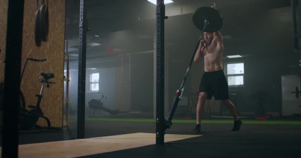 Movimento lento: Homem fazendo exercício de agachamento de minas terrestres de braço único para imprensa. Homem jovem levantando barbell com pesos leves no ginásio — Vídeo de Stock