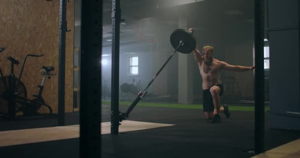 Ένας άντρας που γυμνάζεται στο γυμναστήριο σπρώχνει μια μπάρα νάρκης με το χέρι του ενώ στέκεται στο ένα γόνατο — Αρχείο Βίντεο