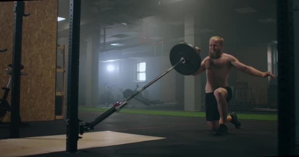 Un luchador masculino que hace ejercicio en el gimnasio empuja un bar de minas terrestres con la mano mientras está de pie sobre una rodilla en cámara lenta — Vídeos de Stock