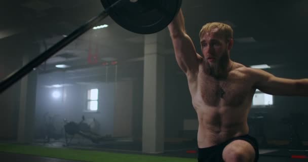 Slow motion: Man doing Single-Arm Landmine Squat-to-Press exercise (en inglés). Hombre joven levantando la barra con pesas ligeras en el gimnasio — Vídeos de Stock