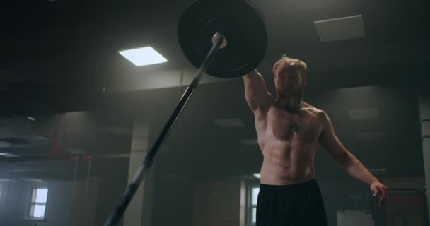 Een mannelijke atleet tilt een halterstang met één hand in slow motion. Krachttraining voor een bokser. De man zweet in de sportschool en oefent de kracht van de klap met zijn hand. — Stockvideo