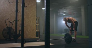Spor salonundaki yorgun erkek sporcu dinleniyor ve egzersiz yapmaya hazırlanıyor. Yavaş çekim terli sporcu derin derin nefes alır ve egzersize konsantre olur.