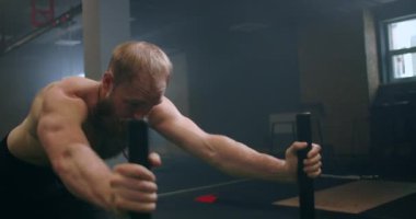 Güçlü bir adam ağır bir yük arabasını ağır çekimde salona itiyor. Vücudunda buhar olan sakallı bir adam.