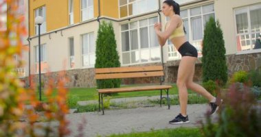 Şehir parkında, alandaki binaların arka planlarına karşı hamleler yapın. Kulaklıkla yavaş çekim ayak eğitimi.