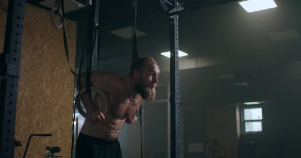 Fitness, culturismo y la gente concepto joven haciendo flexiones en los anillos de gimnasia en el gimnasio. Guapo joven deportista con pierna artificial haciendo flexiones con anillos colgantes de escalera de gimnasia en el gimnasio — Vídeos de Stock