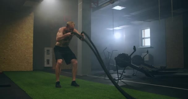 Homem de fitness exercitando com corda de batalha abandonada armazém. Homem duro trabalhando fora no ginásio de treinamento cruzado feito dentro da antiga fábrica . — Vídeo de Stock