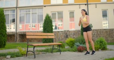 Bir kadın şehir ortamındaki bir parkta kaldırım yolunda hamleler yapıyor. Spor giyim giymiş bir kadının ağır çekimde hamlesini yapıyor.