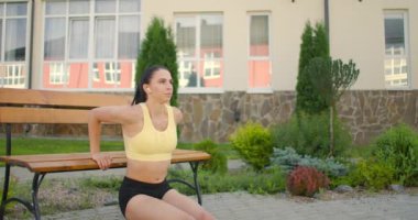 Bir kadın, parkta bir bankın üzerine yavaşça binaların arka planına doğru itiyor. Şehir parkında eğitim