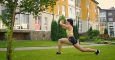 Parktaki bir kadın yeşil çimlerin üzerinde kulaklıkla yoga yapıyor.