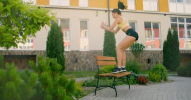Bir kadın, şehir parkında bir bankta ağır çekimde zıplıyor. Yedek kulübesinde yürüyorum. Kentsel bir ortamda eğitim