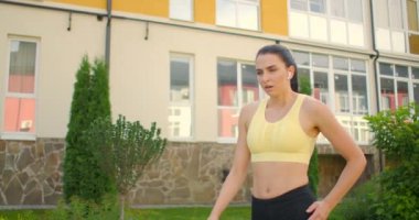 Eğitimden sonra yorgun bir kadın şehir parkında nefes alır ve dinlenir. Kararlı genç kadın derin derin nefes alıyor ve spor yapmaya hazırlanıyor.