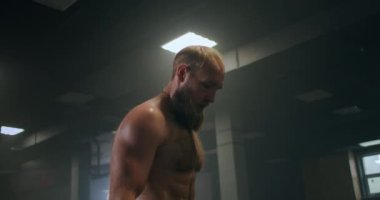 Spor salonundaki yorgun erkek sporcu dinleniyor ve egzersiz yapmaya hazırlanıyor. Yavaş çekim terli sporcu derin derin nefes alır ve egzersize konsantre olur.