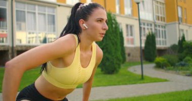 Kulaklıklı yoga dersleri, yazın şehir parkında müzik dinlemek. Eğitimden önce eğim ve ısınma. Çimlerin üzerinde bir kız yoga yapıyor..