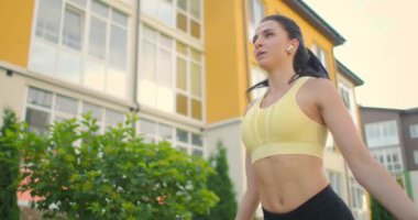 Genç bir kadını şehir ortamında bir eve karşı ip atlamak için eğitmek. Yavaş çekimde parkta ip atlamak. Bir kadın tek başına bir iple antrenman yapar.