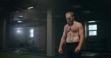Spor salonundaki yorgun erkek sporcu dinleniyor ve egzersiz yapmaya hazırlanıyor. Yavaş çekim terli sporcu derin derin nefes alır ve egzersize konsantre olur.