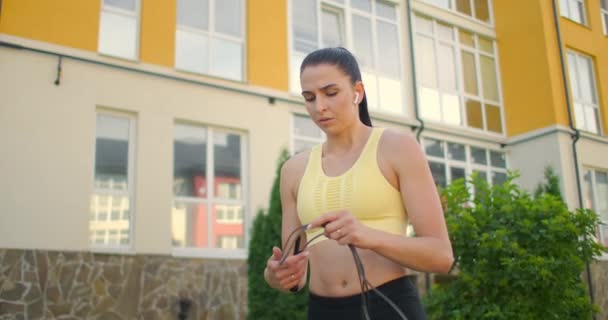 Entrenar a una joven para saltar la cuerda contra una casa en un entorno urbano. Saltar la cuerda en el parque en cámara lenta. Una mujer entrena sola con una cuerda — Vídeos de Stock