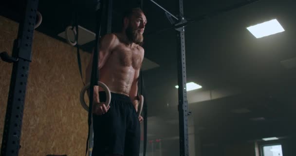 Fuerte barbudo atleta masculino realiza flexiones en anillos de gimnasio en cámara lenta en el gimnasio — Vídeos de Stock