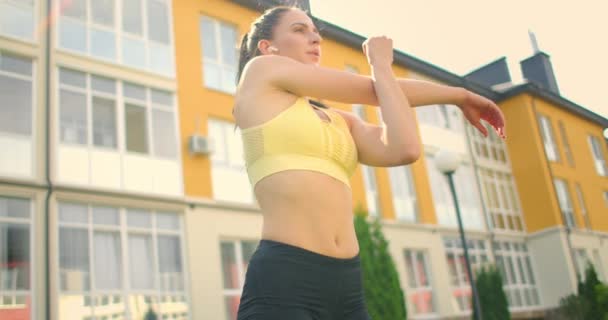 Una mujer joven con auriculares se está estirando en la hierba en un parque de la ciudad en cámara lenta. Escuchar música mientras practicas deportes — Vídeos de Stock