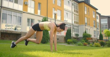 Eğitimden sonra gücünü topluyor. Eğitimden önce kulaklık takan bir kadın parkta ısınıyor. Dışarıya doğru uzanıyor.. 