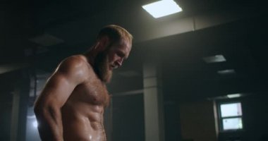 Spor salonundaki yorgun erkek sporcu dinleniyor ve egzersiz yapmaya hazırlanıyor. Yavaş çekim terli sporcu derin derin nefes alır ve egzersize konsantre olur.