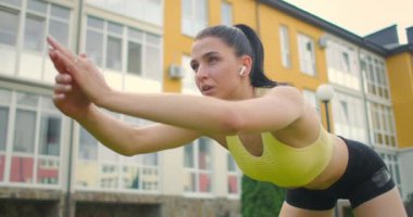 Kulaklıklı genç bir kadın şehrin arka planındaki çimlerin üzerinde yamaçlarda gösteri yapıyor..