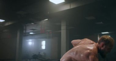 Sakallı bir adam spor salonunda halterle tek eliyle kafasına vurarak antrenman yapıyor. Kara mayını adamı