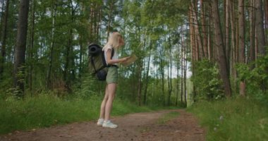 Yol kartı ve pusulayla ormanda patikayı arayan genç bir turist kadının yavaş çekimleri..