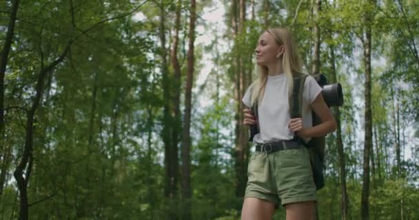 Slow motion porträtt: Vuxen kaukasiska blond kvinna bär shorts och t-shirt vandrar genom skogen. Ung dam vandring — Stockvideo
