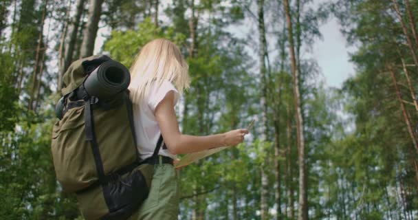 Movimiento lento de una joven turista con una tarjeta de ruta y una brújula en el bosque, en busca del sendero. — Vídeo de stock