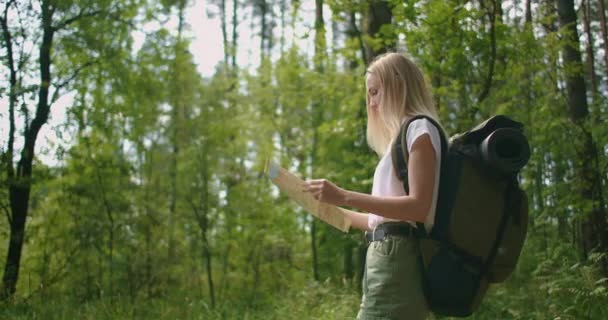 Młoda kobieta podróżnik z mapą i plecakiem relaks na świeżym powietrzu na szlaku przyrody w letni dzień wakacji. Koncepcja wędrówki po świecie. Wycieczka. Kierunek wyboru z mapą. — Wideo stockowe