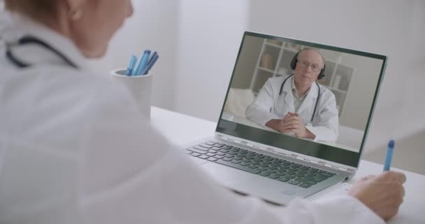 Chefarzt des Krankenhauses kommuniziert mit Ärzten per Videokonferenz, Frau listet ihn auf und macht Notizen — Stockvideo