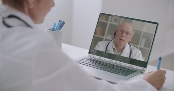 Professor de medicina está treinando profissionais de saúde on-line, médico mulher está ouvindo sua palestra por laptop e escrever notas — Vídeo de Stock