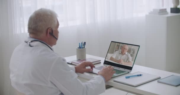 Старик звонит семейному врачу по видеосвязи, чтобы проконсультироваться о здоровье и лечении, телемедицине — стоковое видео